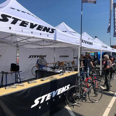 Weißer 3x3 m Eventzelt mit Stevens-Bikes-Logo für eine Radsportveranstaltung mit schwarzen halbhohen Seitenwänden und Theken