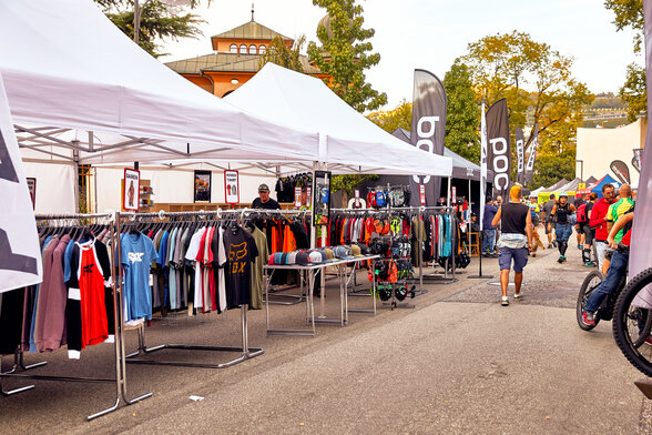 Die weißen Promotionzelte dienen als Verkaufszelt auf einem Event. Unter dem Faltpavillon hängen verschiedene T-shirts.