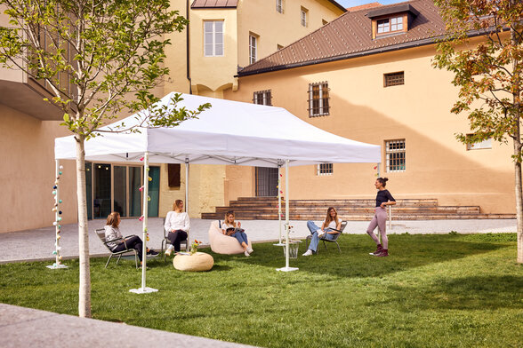 The 6x3 m folding gazebo serves as an outdoor canopy for a library. Young people sit under it.