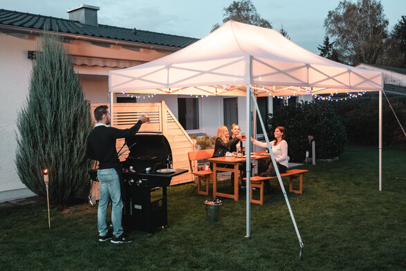 Friends celebrate a barbecue and garden party under the garden tent. The garden tent is festively decorated with fairy lights.