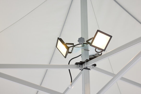 The LED spotlight, consisting of 3 spots, is mounted on the central pole of the folding gazebo. The LED spotlight is on.