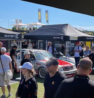 Auf einem Automobil-Event steht ein silbernes, bedrucktes Auto unter einem schwarzen, bedruckten Ecotent Faltpavillon Serie E1 der Größe 4,5 x 3 Meter.